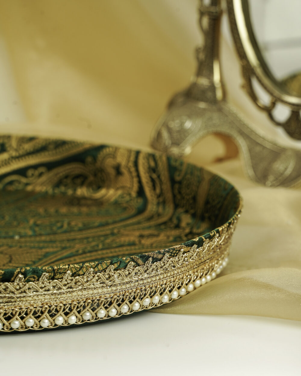 A close-up of the Baagh Shagun Thaal with Cover by Navka Studio, detailing its rich green paisley brocade, gold lace, and pearl trim.